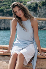 Blusa larga de fit fluido, cuello halter, sin mangas, bajo asimétrico, plisados en costado con abertura y nudo decorativo , cierre posterior con botón y ojal.