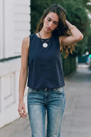 Blusa básica de cuello redondo, sin mangas, fit recto, costura frontal, cierre posterior con botón y ojal.