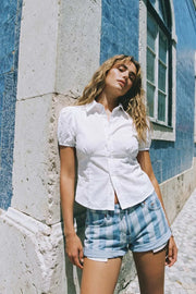 Camisa corta de fit recto, manga corta abullonada con rib elástico en bordes, cuello camisero, cortes y plisados frontales. Cierre frontal con hilera de botones.