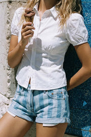 Camisa corta de fit recto, manga corta abullonada con rib elástico en bordes, cuello camisero, cortes y plisados frontales. Cierre frontal con hilera de botones.