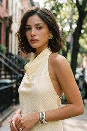 Blusa de estampado cuadros, cuello halter fluido, escote en espalda con lazo amarrable posterior, cierre con botón y ojal.