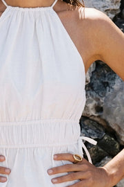 Top corto de cuello halter con plisados, tirantes delgados, detalle de rib con plisados y lazos laterales en costados, peplum con olanes en bajo y cierre posterior con botón y ojal.
