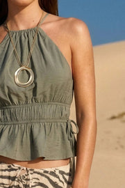 Top corto de cuello halter con plisados, tirantes delgados, detalle de rib con plisados y lazos laterales en costados, peplum con olanes en bajo y cierre posterior con botón y ojal.