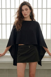 Blusa tipo capa con manga seguida, bajo asimétrico, cuello redondo y escote en espalda. Cierre posterior con botón y ojal.
