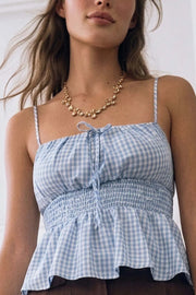 Top corto de tirantes delgados ajustables, estampado cuadros, escote redondeado con plisados y lazo frontal decorativo, fruncido en cintura y peplum de olanes en bajo. Detalle de rib elástico posterior.