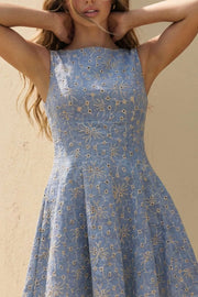 Vestido corto de cuello barco, sin mangas, pinzas frontales, corte en a y olanes en bajo. Detalle de bordado con perforado en tejido, escote en espalda y cierre lateral con cremallera oculta.