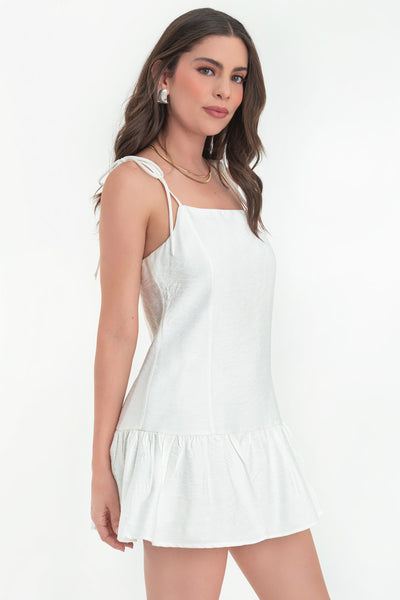 Vestido corto de fit fluido, tirantes delgados con nudo amarrable, escote recto, costuras frontales, corte en cadera y bajo con olanes. Cierre posterior con cremallera oculta.