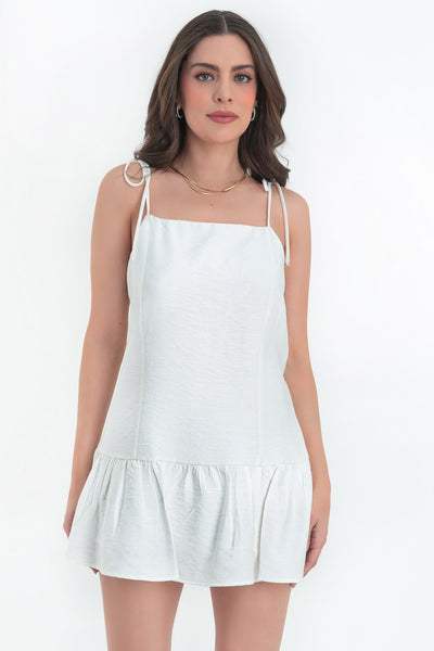 Vestido corto de fit fluido, tirantes delgados con nudo amarrable, escote recto, costuras frontales, corte en cadera y bajo con olanes. Cierre posterior con cremallera oculta.