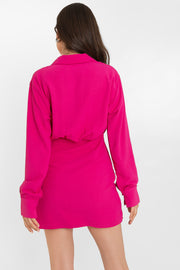 Vestido corto de manga larga con puño abotonado, escote v cruzado con detalles plisados, cuello camisero, fit ajustado y plisado lateral con bajo curveado frontal. Cierre lateral con cremallera oculta.