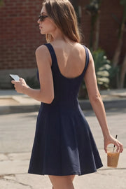 Vestido corto de cuello barco, sin mangas, cortes frontales, escote en espalda y corte en a con olanes en bajo.