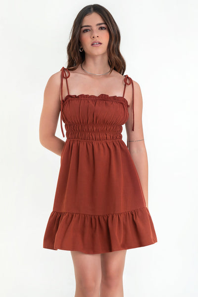Vestido corto de escote recto con plisados, rib y olanes en borde, tirantes delgados con nudo amarrable, fruncido con rib elástico y plisados en cintura, corte en a y bajo con olanes en borde.