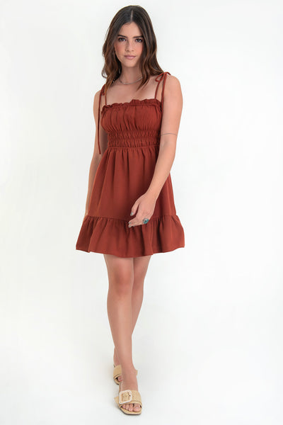 Vestido corto de escote recto con plisados, rib y olanes en borde, tirantes delgados con nudo amarrable, fruncido con rib elástico y plisados en cintura, corte en a y bajo con olanes en borde.