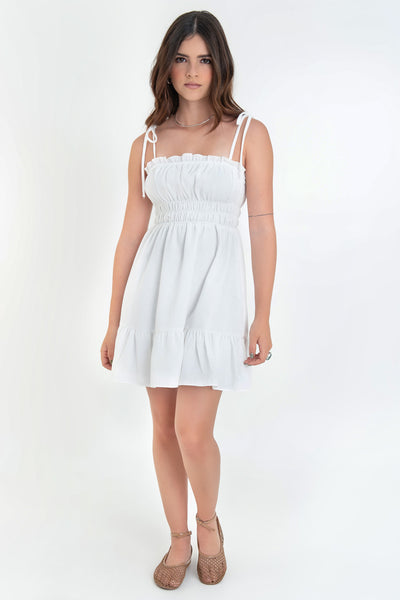 Vestido corto de escote recto con plisados, rib y olanes en borde, tirantes delgados con nudo amarrable, fruncido con rib elástico y plisados en cintura, corte en a y bajo con olanes en borde.