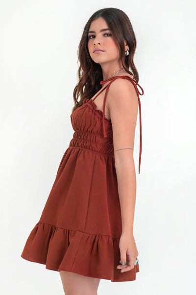 Vestido corto de escote recto con plisados, rib y olanes en borde, tirantes delgados con nudo amarrable, fruncido con rib elástico y plisados en cintura, corte en a y bajo con olanes en borde.