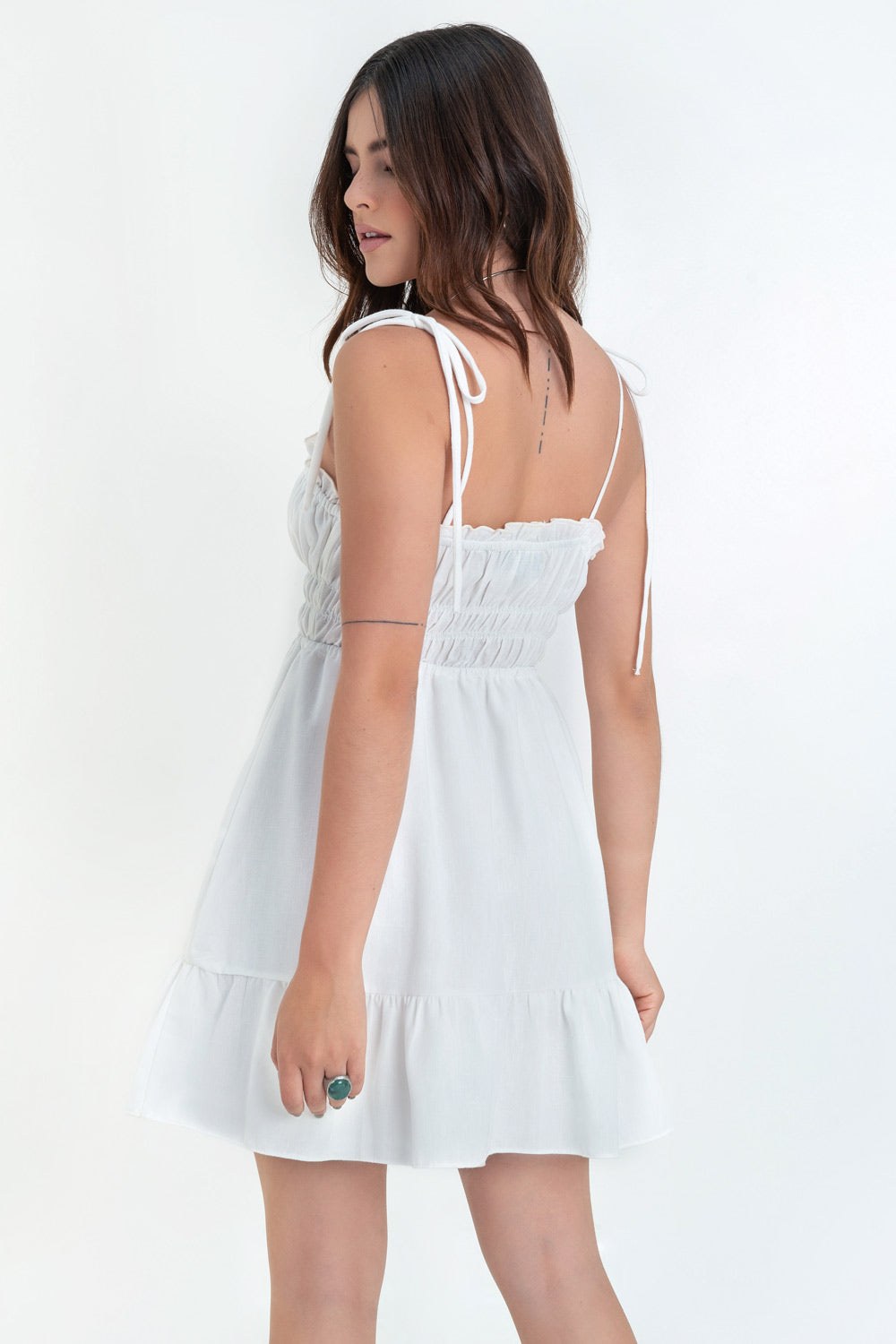 Vestido corto de escote recto con plisados, rib y olanes en borde, tirantes delgados con nudo amarrable, fruncido con rib elástico y plisados en cintura, corte en a y bajo con olanes en borde.