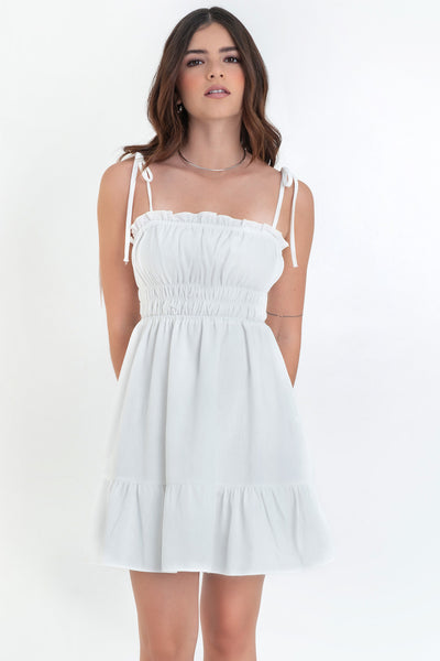 Vestido corto de escote recto con plisados, rib y olanes en borde, tirantes delgados con nudo amarrable, fruncido con rib elástico y plisados en cintura, corte en a y bajo con olanes en borde.