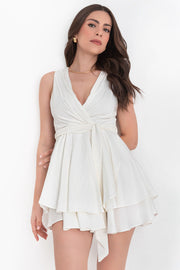 Vestido corto sin mangas, escote v cruzado con plisados decorativos frontales, corte en a, pretina con trabillas y cinturón amarrable del mismo tejido. Detalle de bajo con capas de olanes y cierre posterior con cremallera oculta.