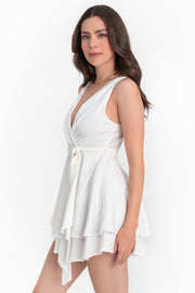 Vestido corto sin mangas, escote v cruzado con plisados decorativos frontales, corte en a, pretina con trabillas y cinturón amarrable del mismo tejido. Detalle de bajo con capas de olanes y cierre posterior con cremallera oculta.