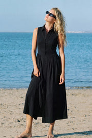 Vestido midi camisero, de corte en a, sin mangas, cuello camisero, cortes decorativos con plisados en cadera, pinzas y cierre frontal con hilera de botones.