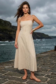 Vestido midi de estampado cuadros, tirantes delgados con nudo amarrable, escote recto, pinzas frontales y corte en a con olanes en bajo. Cierre posterior con cremallera oculta.
