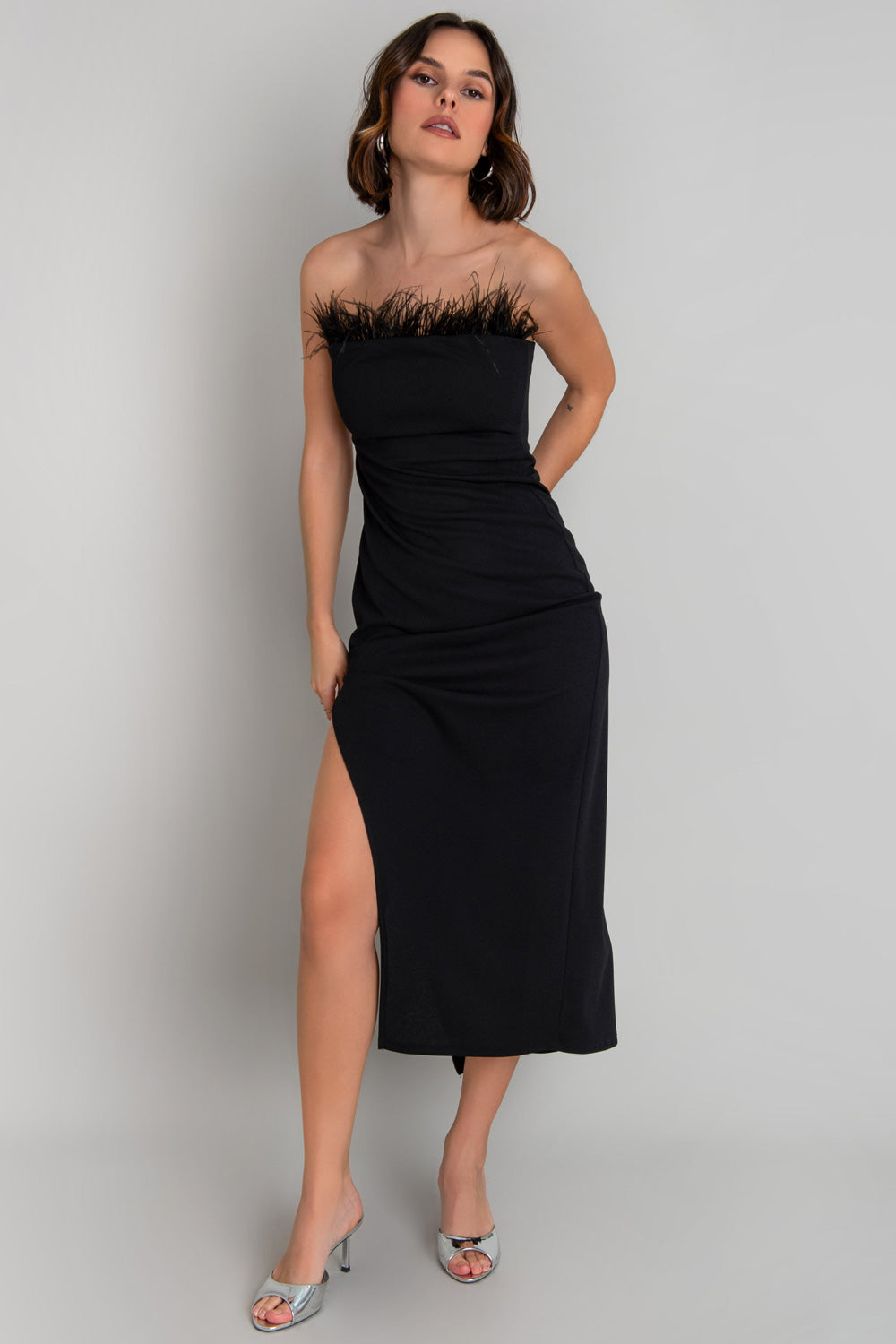 Vestido midi strapless, de fit ajustado, escote recto con detalle decorativo de plumas en borde y abertura lateral en bajo. Cierre posterior con cremallera visible en contraste.