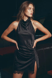 Vestido mini satinado, de cuello halter fluido, escote en espalda, fit fluido, sin mangas, plisados laterales y encaje decorativo en borde de bajo. Cierre posterior con broches ocultos. Detalle de abertura decorativa en bajo.