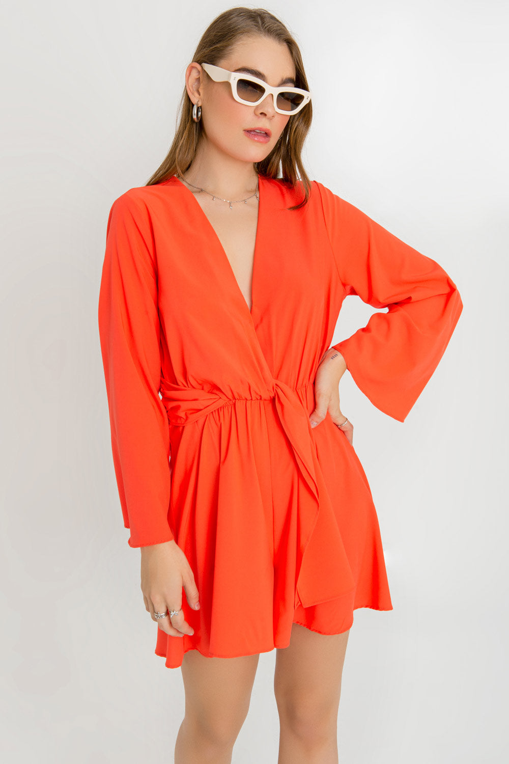 Playsuit de manga larga amplia, escote v cruzado, plisado en cintura con rib elástico y lazo amarrable frontal. Detalle de escote en espalda, bajo con olanes y cierre con botón, ojal y cremallera oculta. 